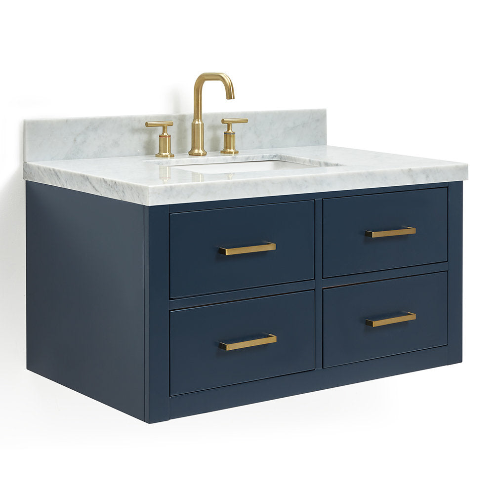 Wall-mounted modern solid wood bathroom vanity with navy cabinet, white stone marble top and integrated undermount sink, shown with brushed brass faucet and matching brass drawer pulls.