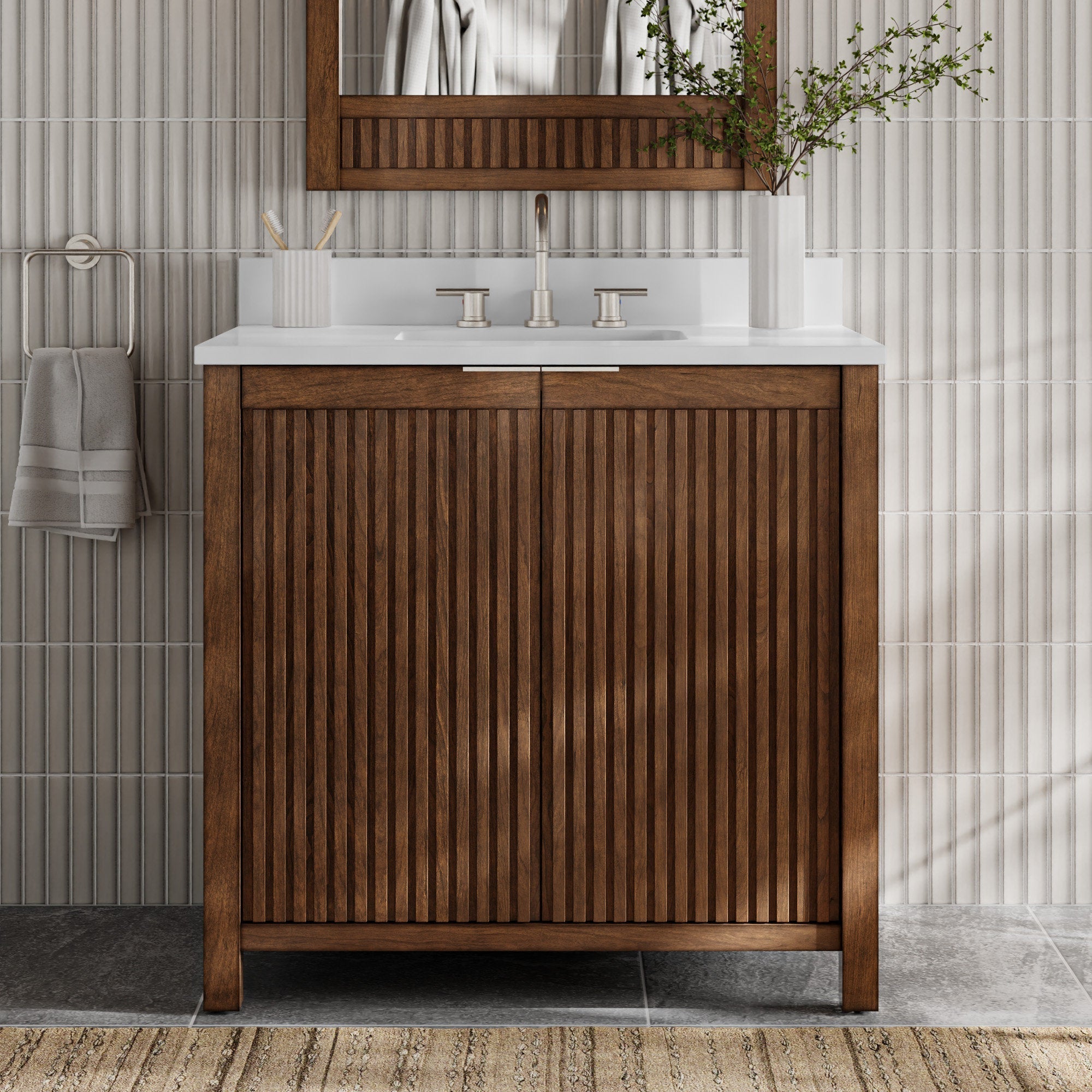 Freestanding modern single-sink bathroom vanity in warm solid wood with fluted vertical doors, stone-colored countertop with integrated white sink, brushed nickel faucet, wood-framed mirror, towel ring and vase of greenery.