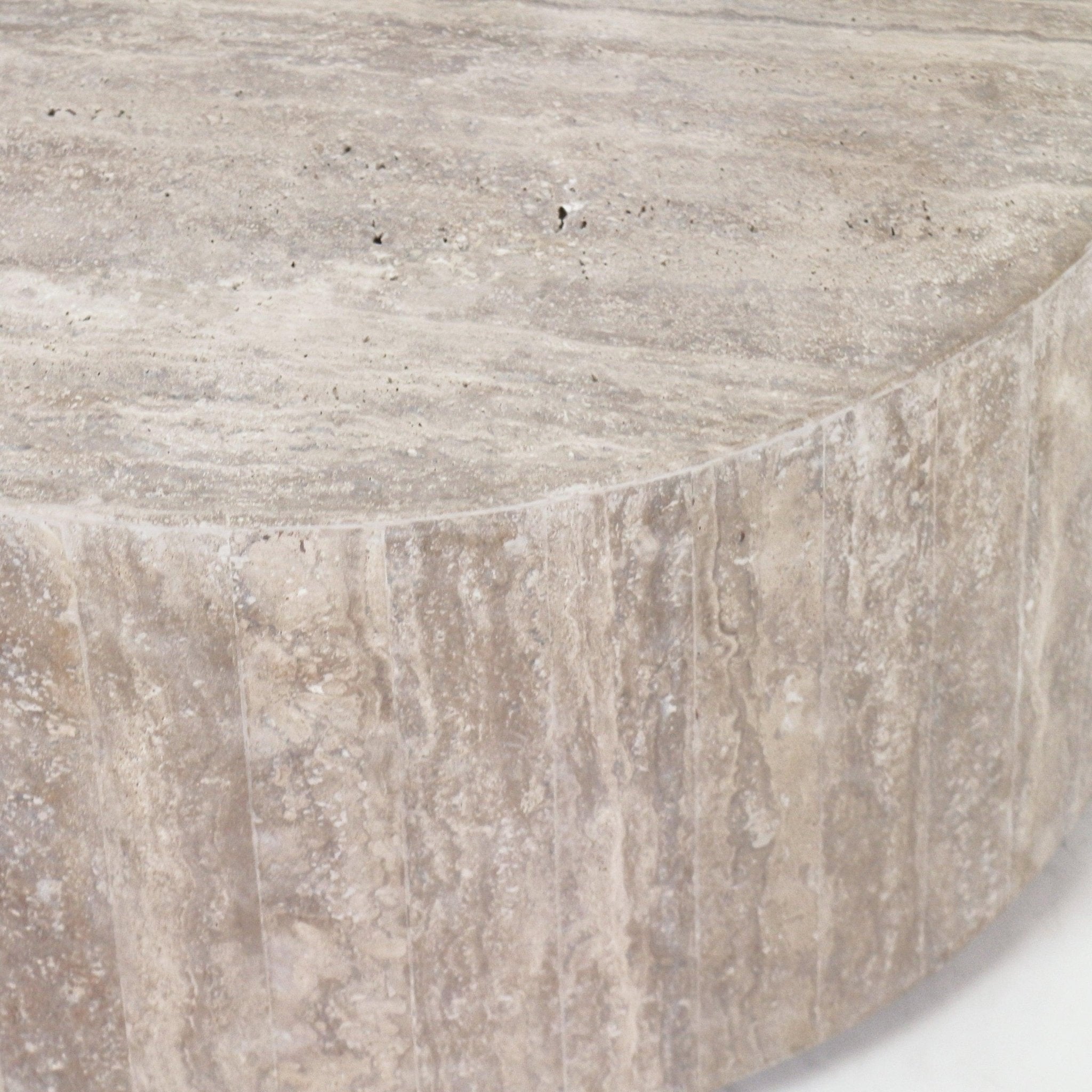 Close-up of a round travertine coffee table top and curved edge, showing natural beige stone veining and textured vertical striations.