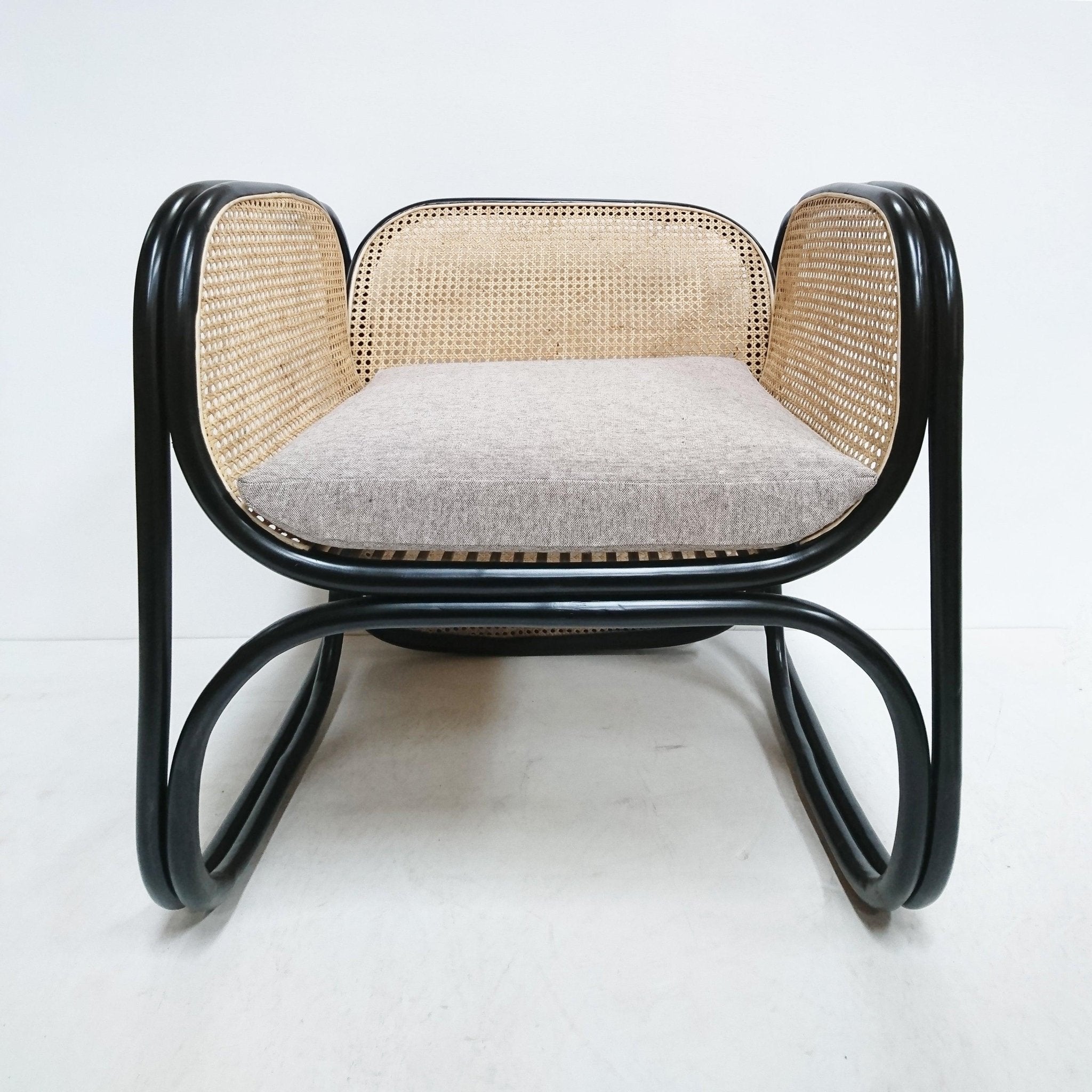 Front view of a modern lounge chair with a black curved bentwood frame, natural woven cane back and sides, and a light gray fabric seat cushion.