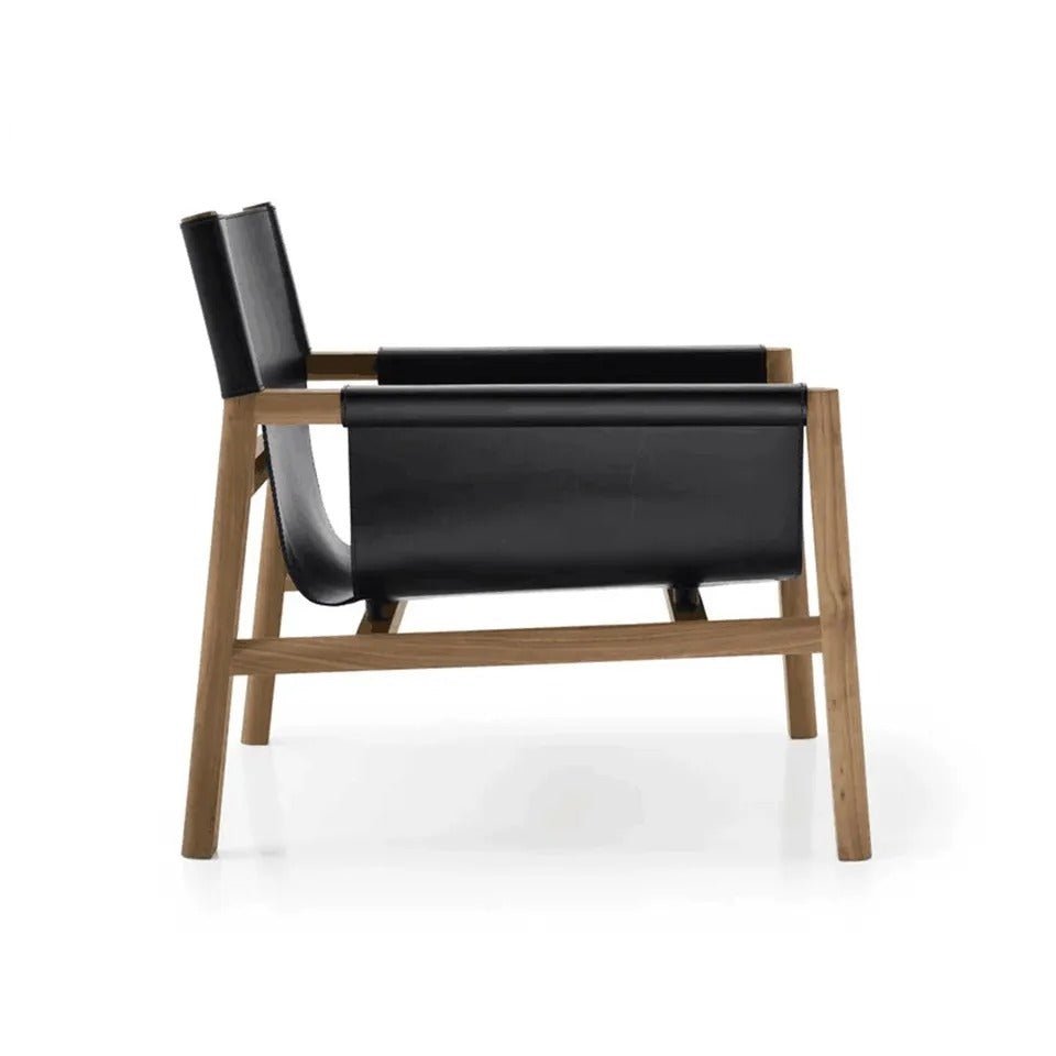 Side view of a mid-century modern accent lounge chair with a natural teak wood frame and black leather sling seat and backrest, showing angled legs and exposed joinery on a white background.