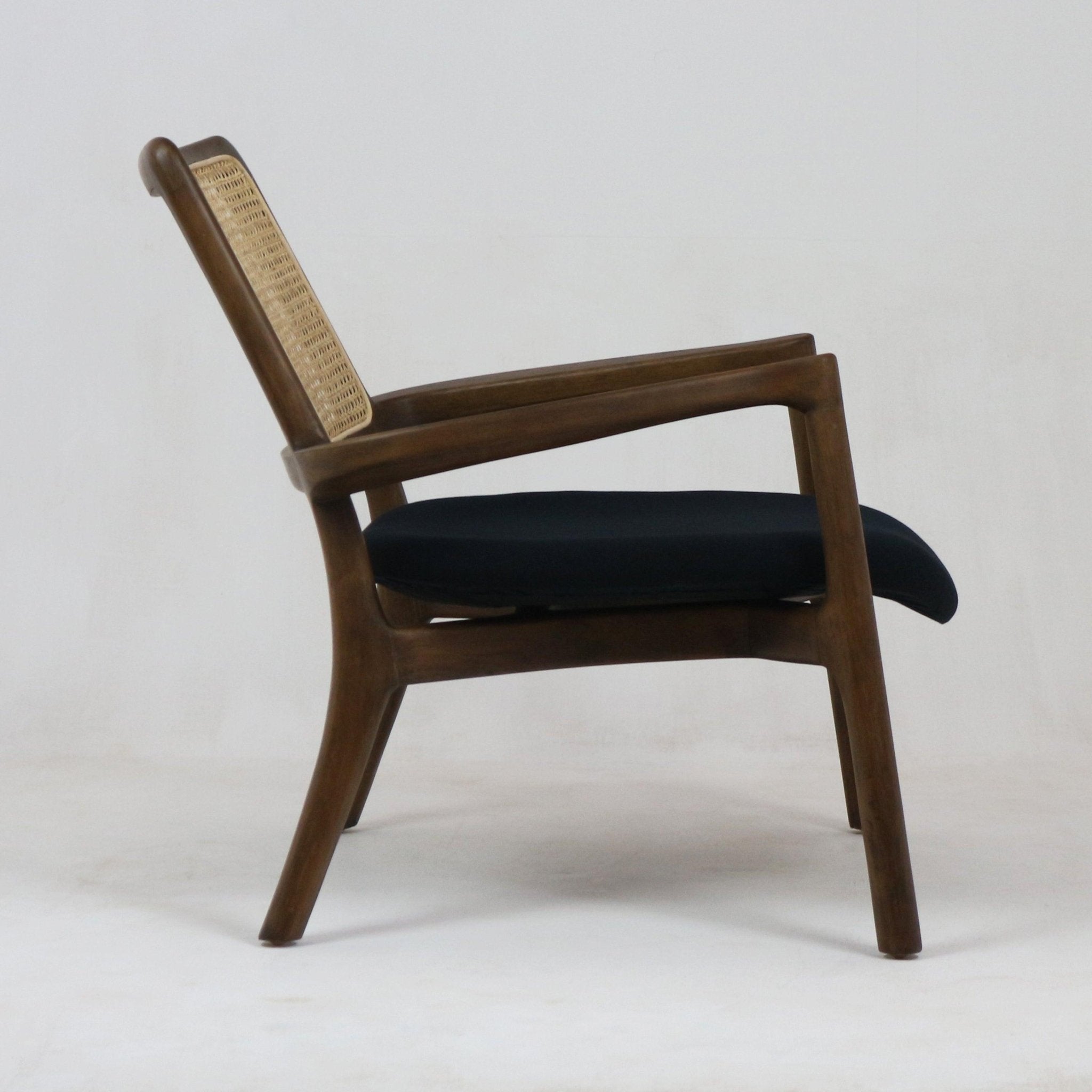 Side profile of a mid-century modern teak lounge chair featuring a woven cane backrest and a dark fabric seat cushion on a neutral background.