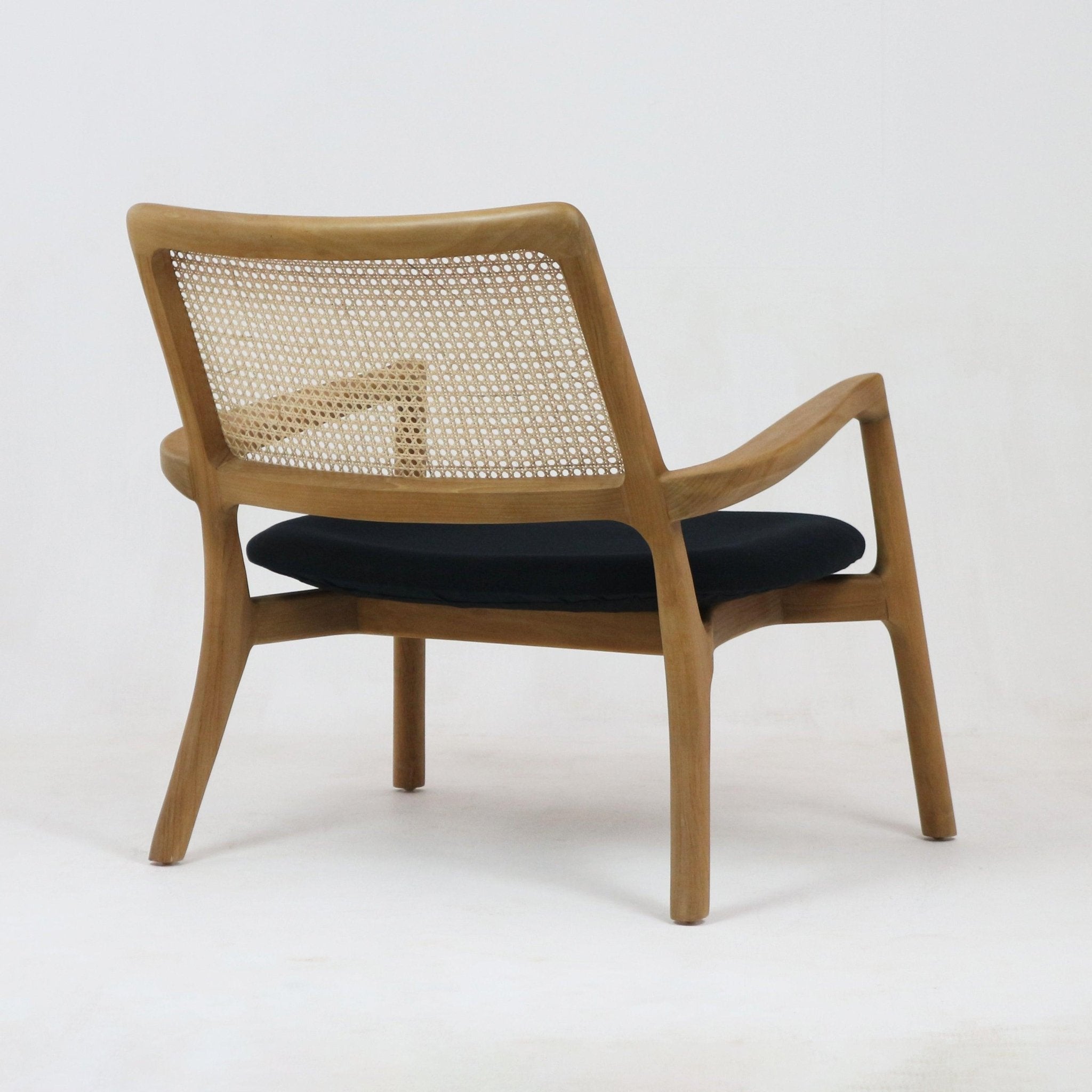 Rear three-quarter view of a mid-century modern teak lounge chair featuring a solid teak frame, woven cane backrest and a black upholstered fabric seat cushion.