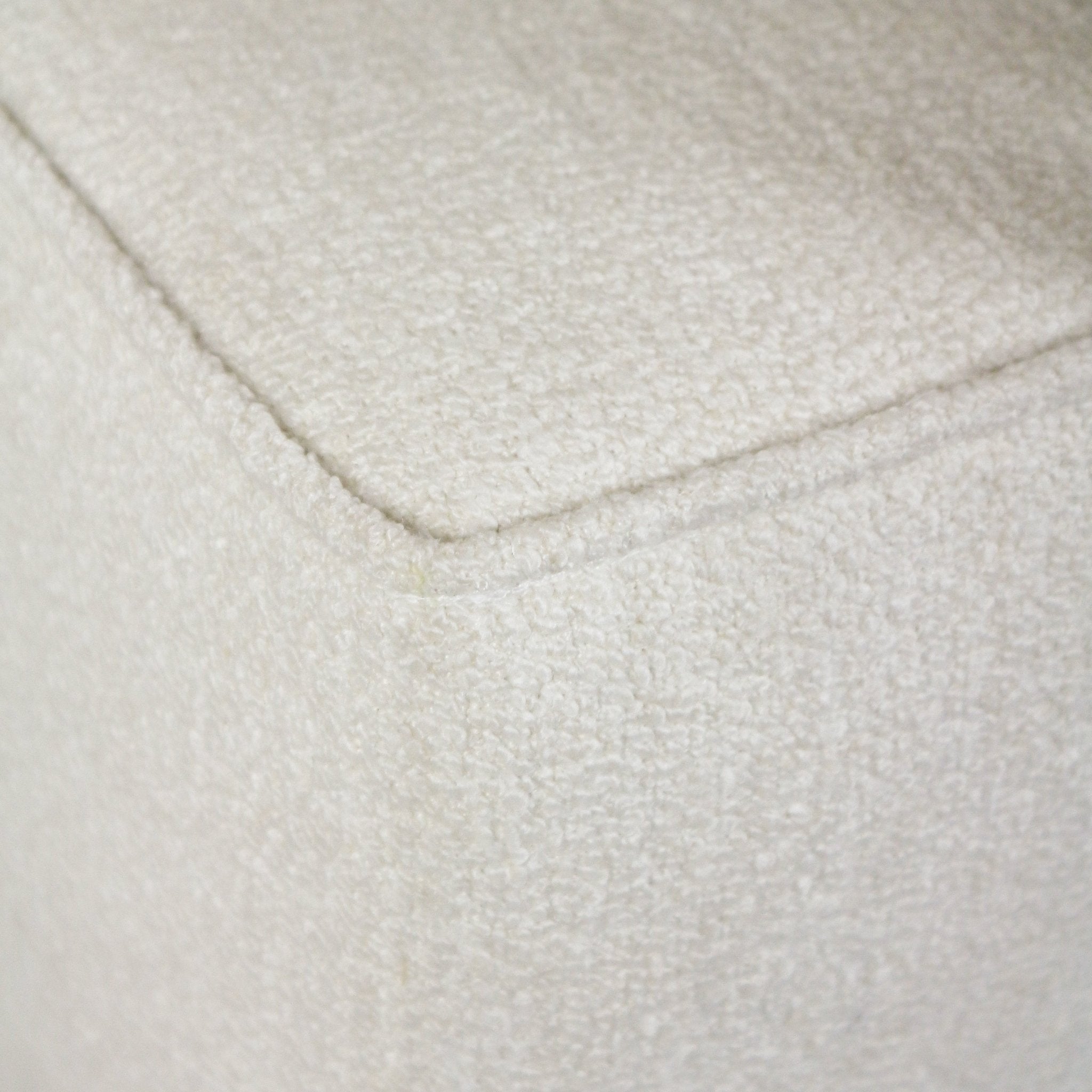 Close-up of a white boucle upholstered bench corner showing the piped edge and textured looped fabric.