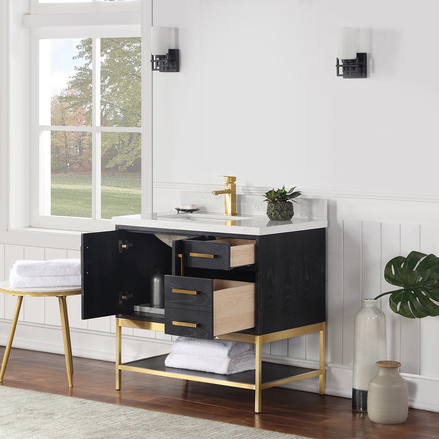 Modern 36-inch black solid wood single-sink bathroom vanity with white stone countertop and ceramic basin, open drawers and cabinet, gold brass faucet and metal base, styled with a small plant and folded towels.