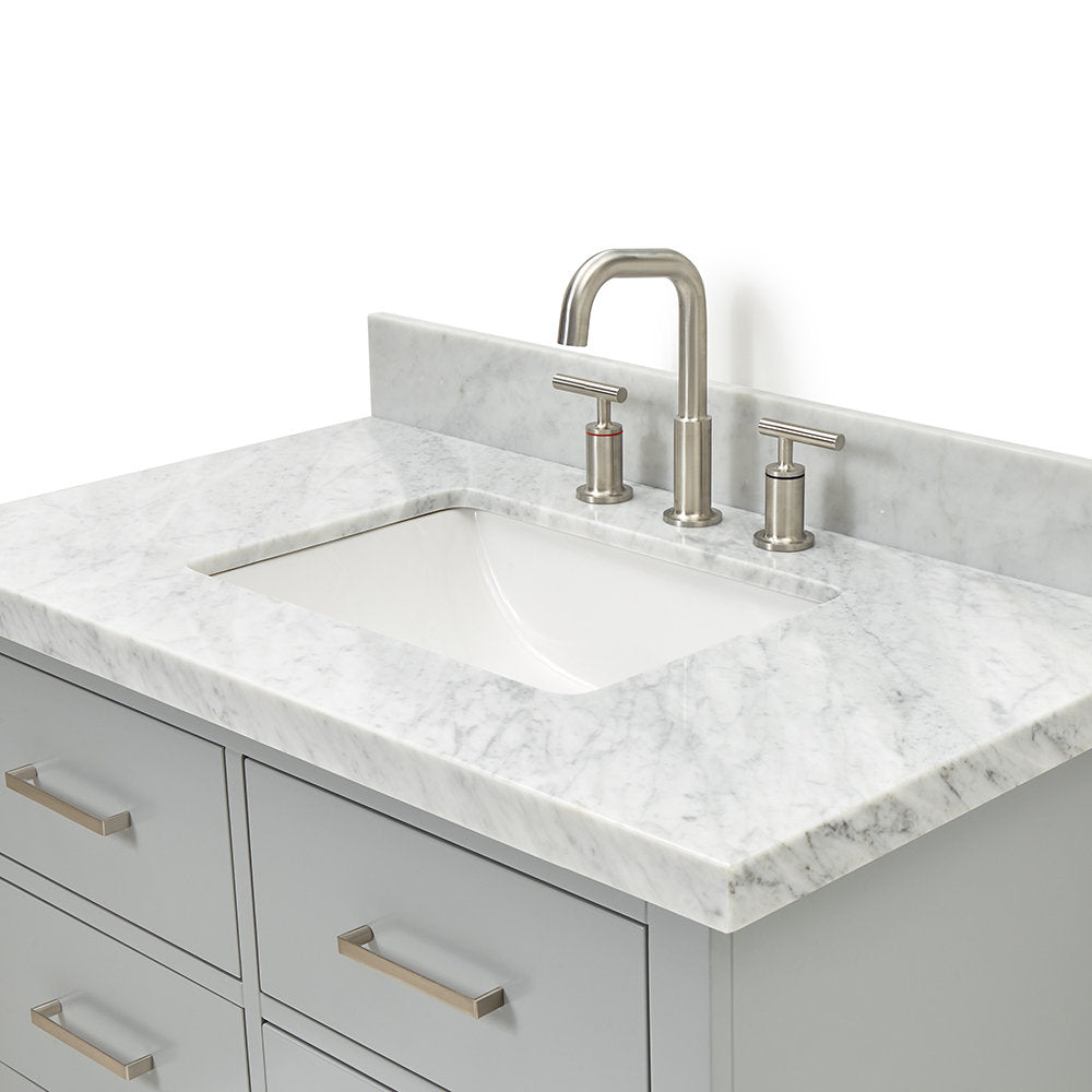 Modern gray solid wood vanity with a stone countertop and single undermount white ceramic sink, paired with a brushed nickel widespread faucet, matching metal drawer pulls, and a short stone backsplash.
