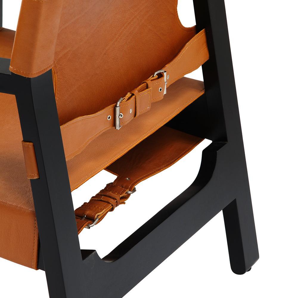 Close-up of tan leather seat and back straps with metal buckles attached to a matte black solid wood frame of a modern lounge chair.