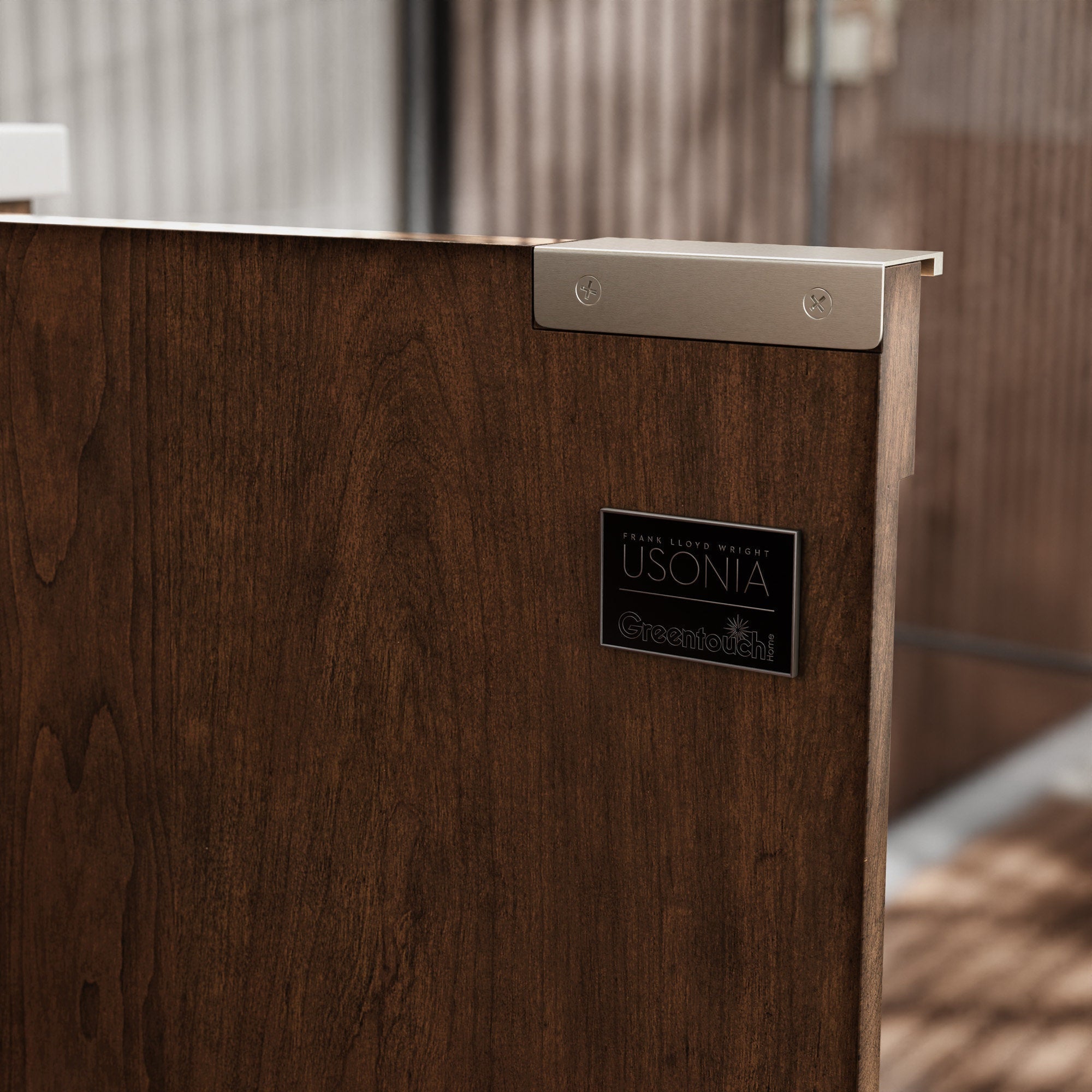 Close-up of a dark natural solid wood bathroom vanity side showing rich wood grain, a satin metal corner bracket, and a small rectangular black logo plate beneath the light stone countertop edge.