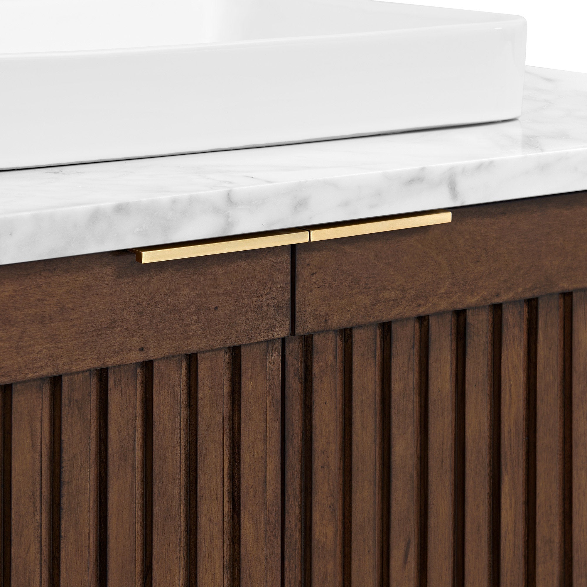 Close-up of a modern fluted solid wood bathroom vanity in warm brown, featuring a stone marble countertop, the edge of a white rectangular ceramic vessel sink, and slim brushed brass bar handles.