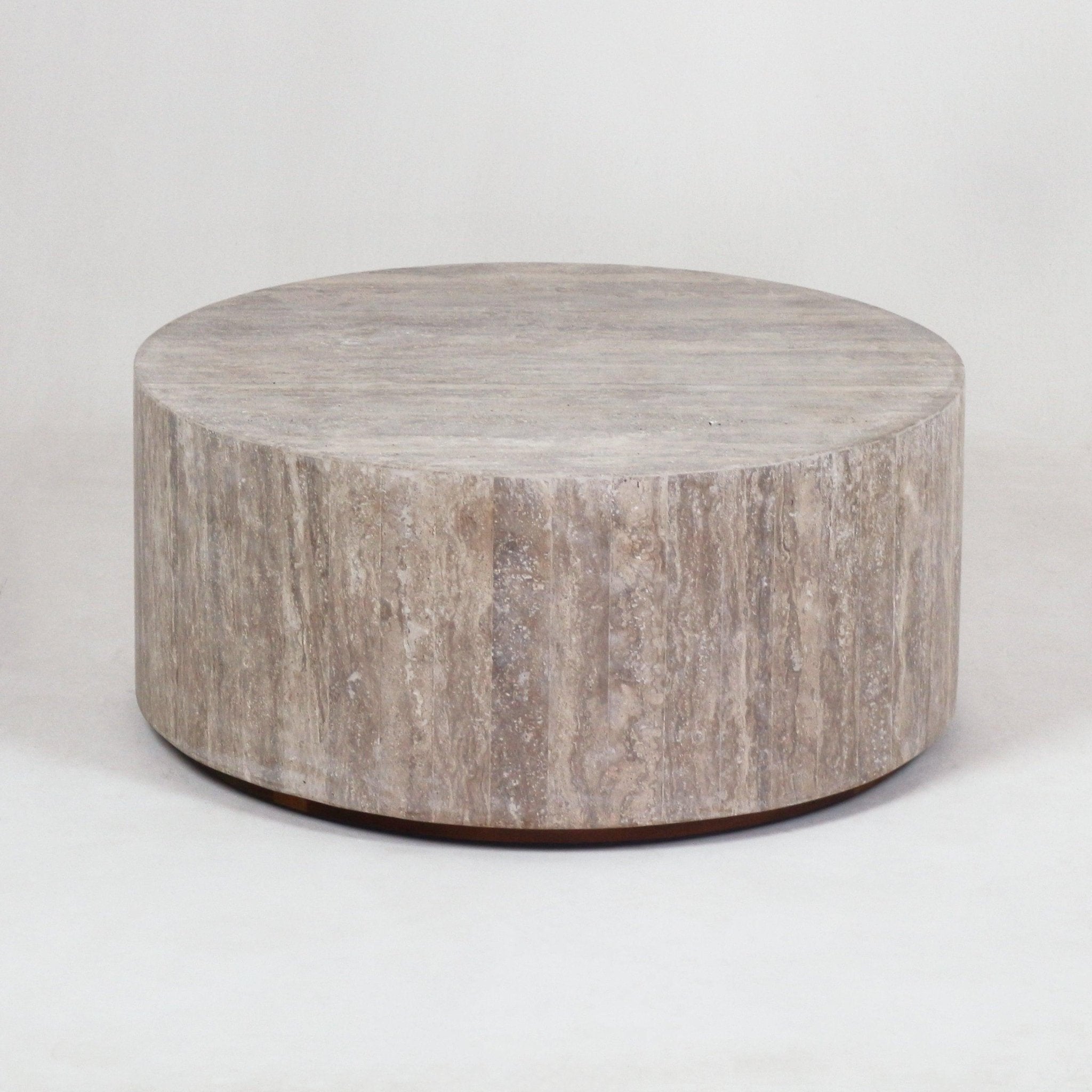 Low round travertine coffee table in natural beige with cylindrical drum shape, visible stone veining and a recessed dark base, modern minimalist design for living or outdoor seating areas.