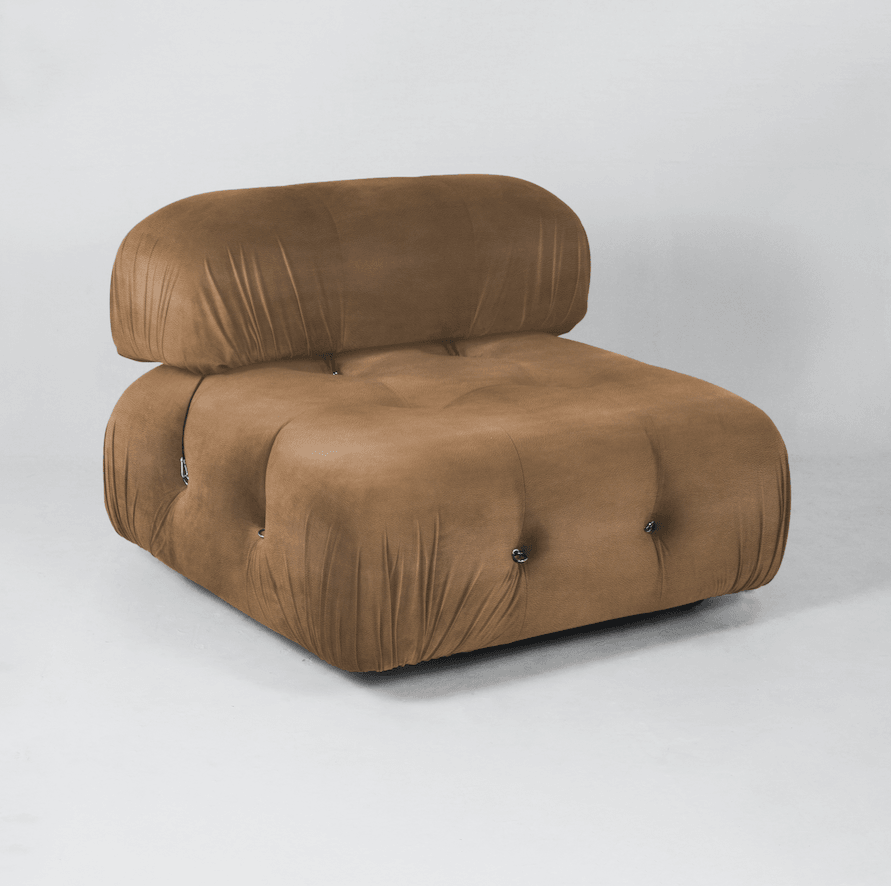 Armless tan leather modern sofa chair with a low rounded back, deep tufted seat and gathered upholstery details, photographed against a neutral studio background.