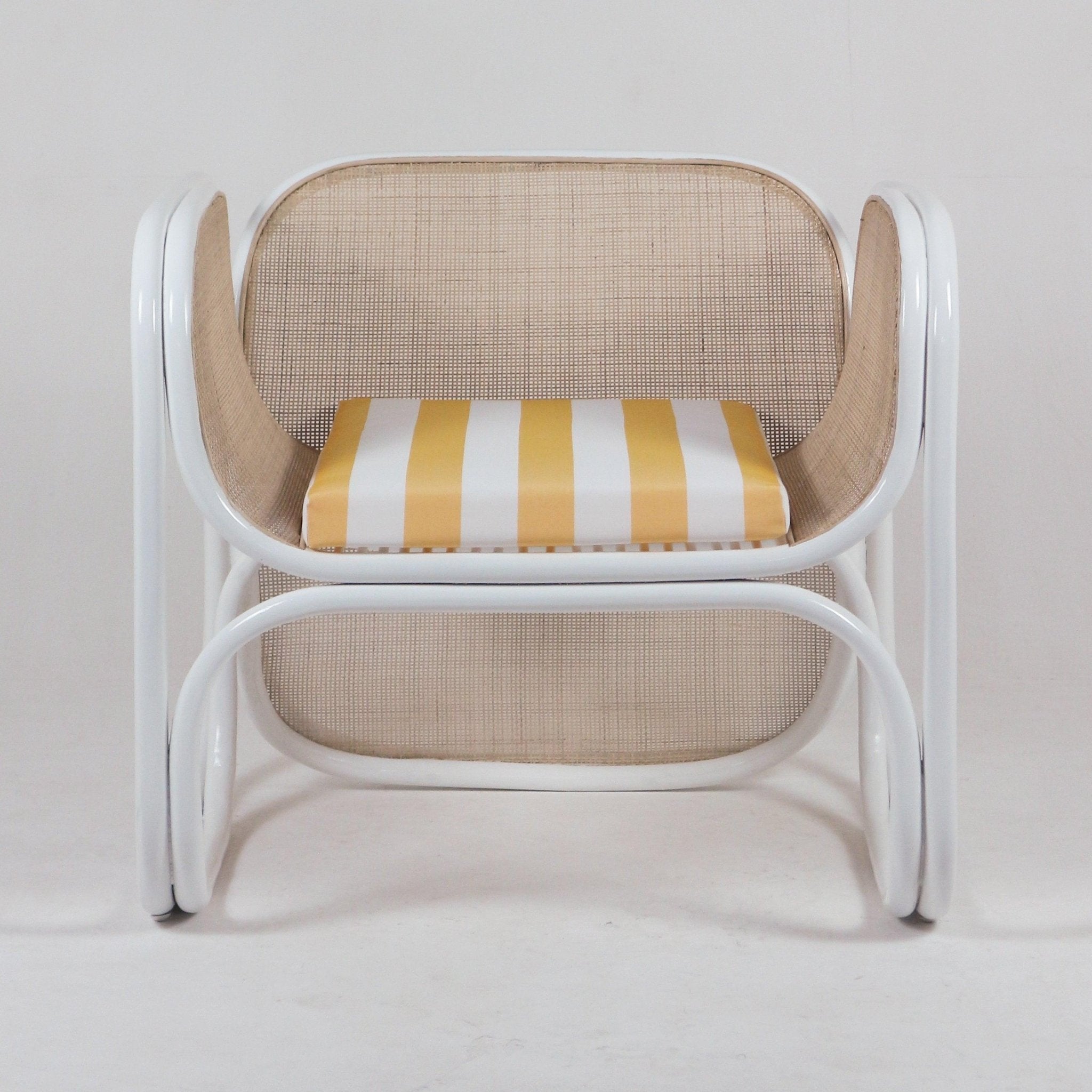 Modern lounge chair with a white metal tubular frame, woven natural cane back and arms, and a striped yellow-and-white fabric seat cushion.