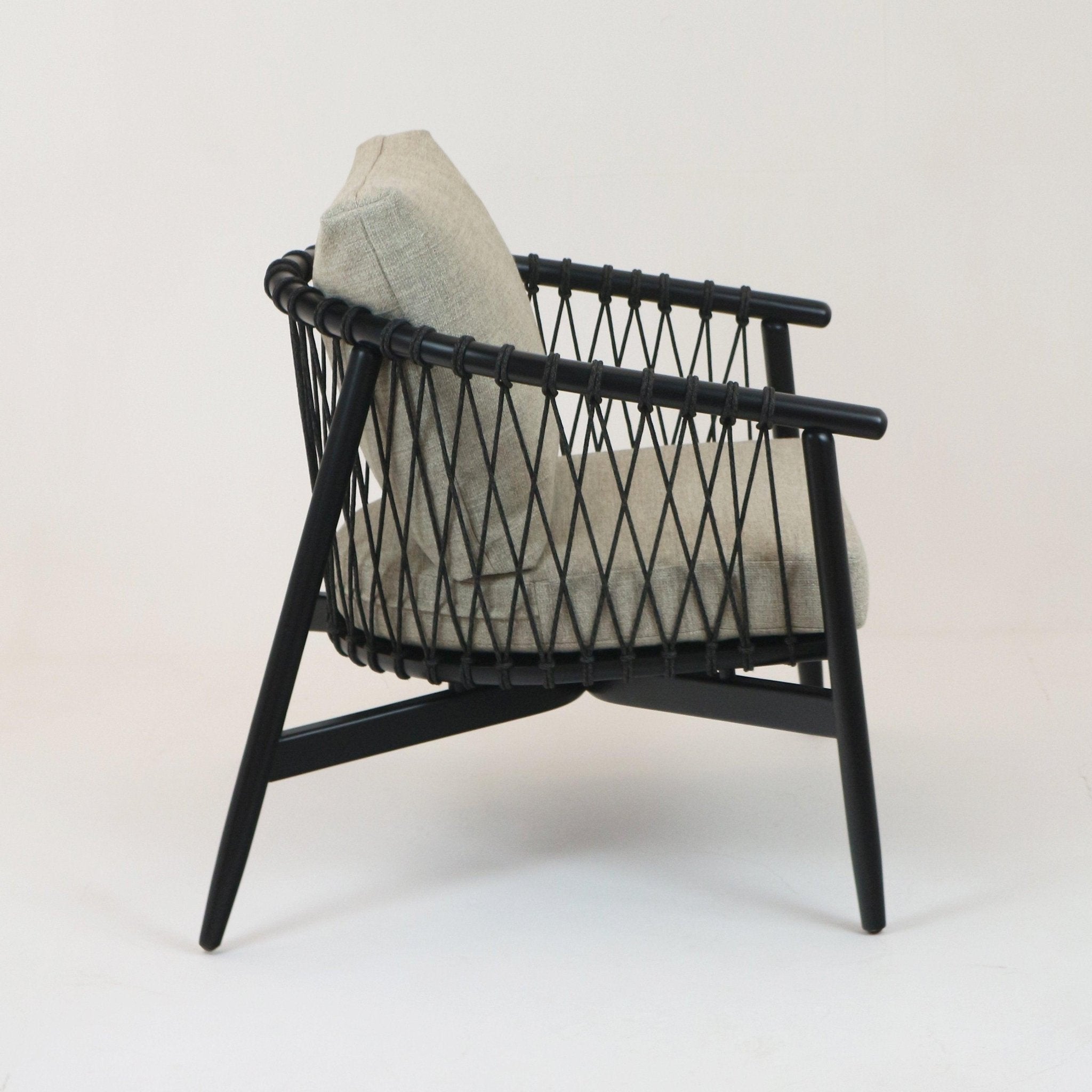 Side view of a modern lounge chair with a beige alpaca boucle cushion set in a black solid wood frame featuring wrapped rope lattice back and slender angled legs.