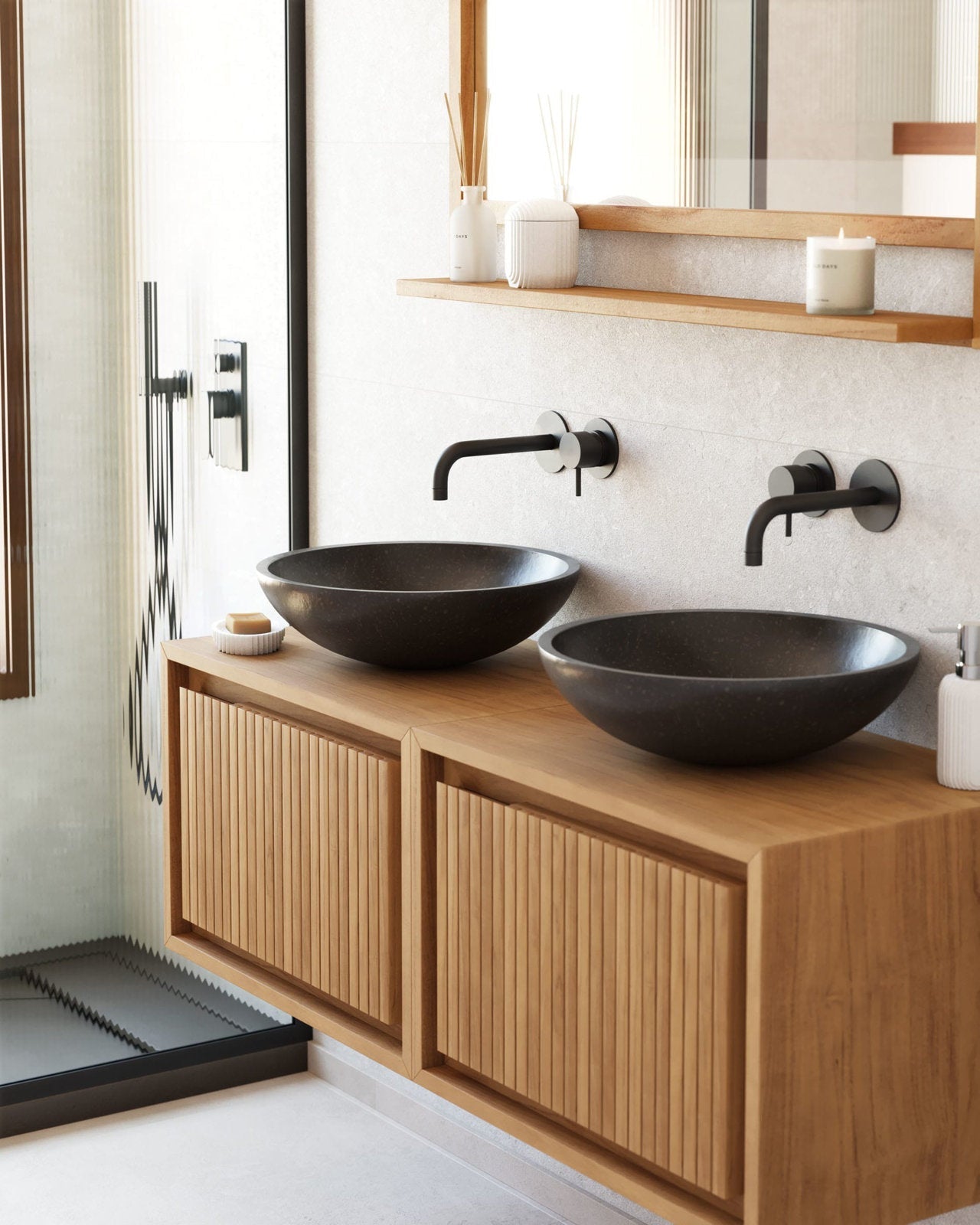 Floating solid wood bathroom vanity with two dark stone vessel sinks, matte black wall-mounted faucets, slatted wood cabinet doors and a narrow wood shelf styled with a candle and diffuser against a light stone wall.