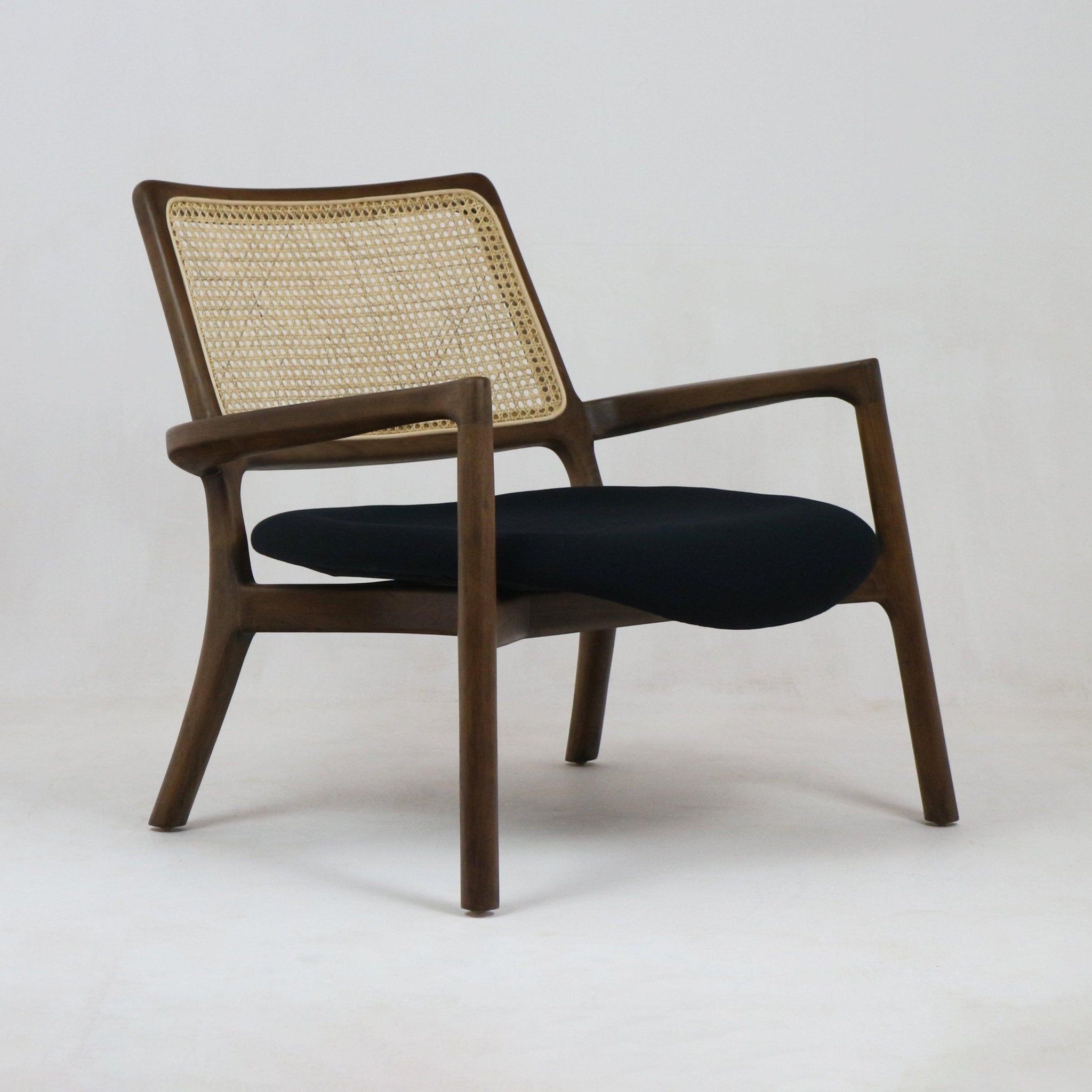 Mid-century modern teak lounge chair with a woven cane back and black fabric upholstered seat, low solid wood frame and curved armrests shown on a neutral background.