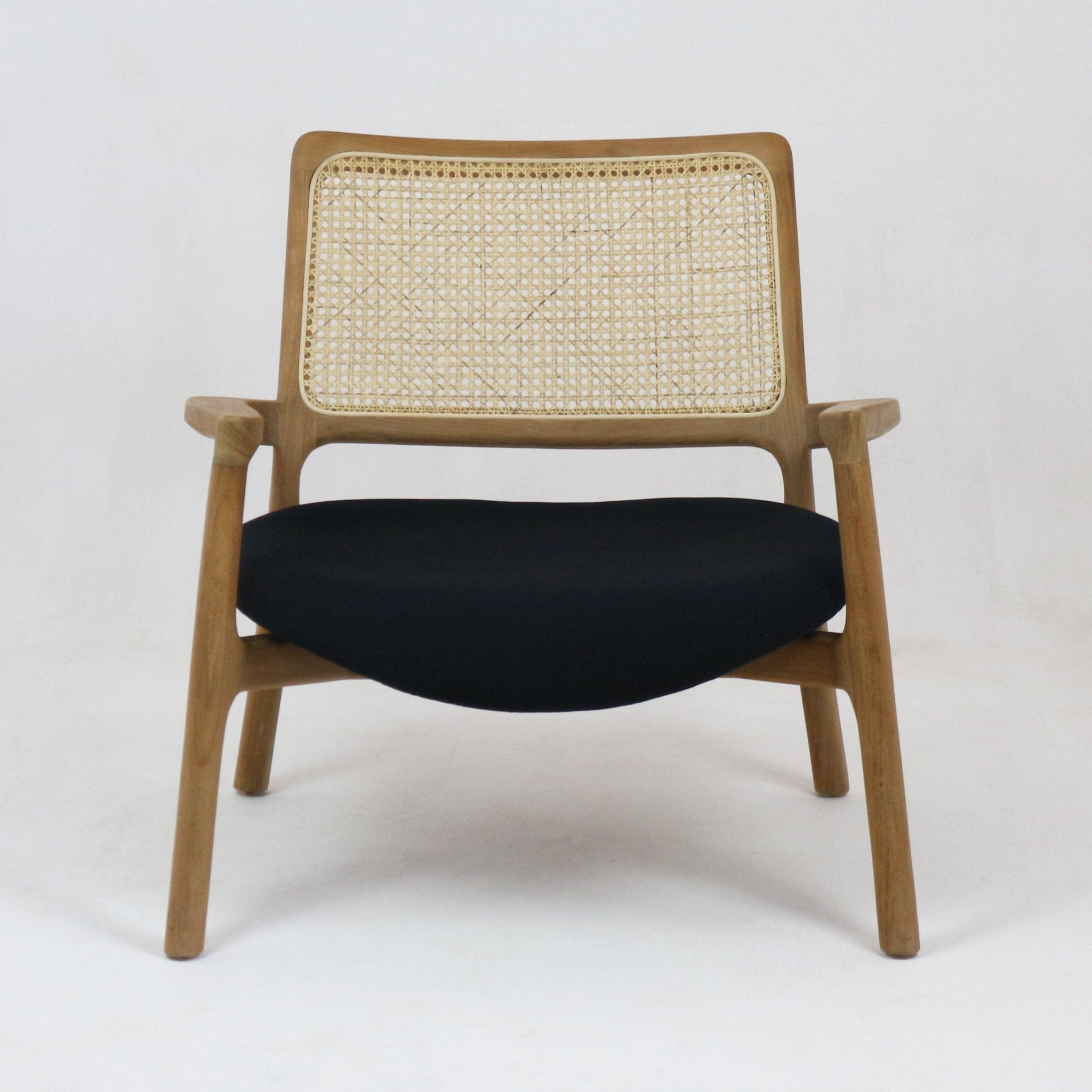 Mid-century modern lounge chair with a teak wood frame, woven cane backrest, slim wooden arms and a low black fabric upholstered seat shown front-facing on a plain white background.