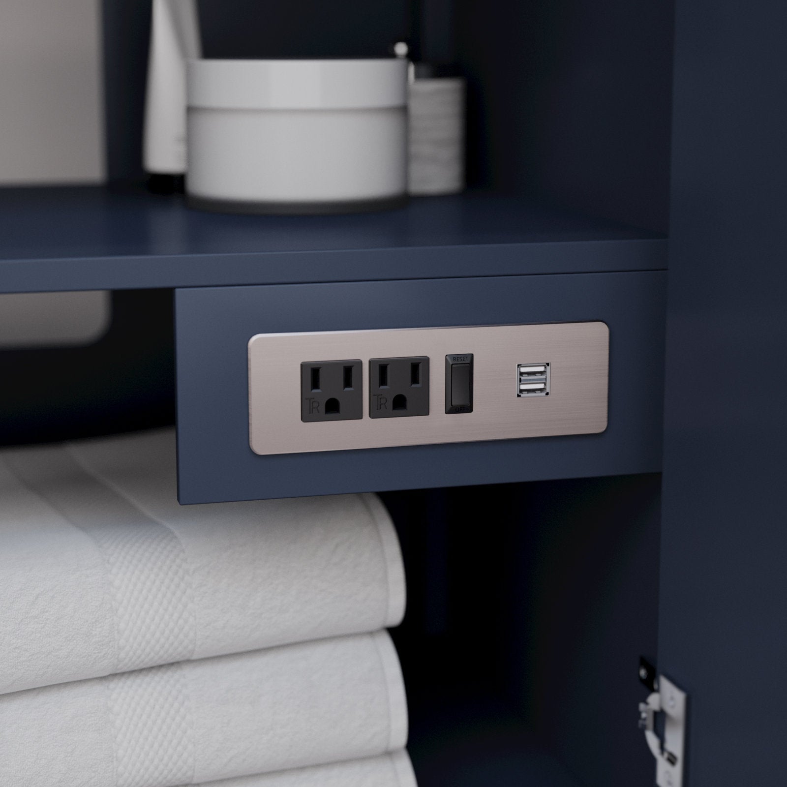 Close-up of a brushed-nickel power panel with two grounded outlets, a reset switch and dual USB ports installed inside a dark blue solid wood vanity above folded white towels.