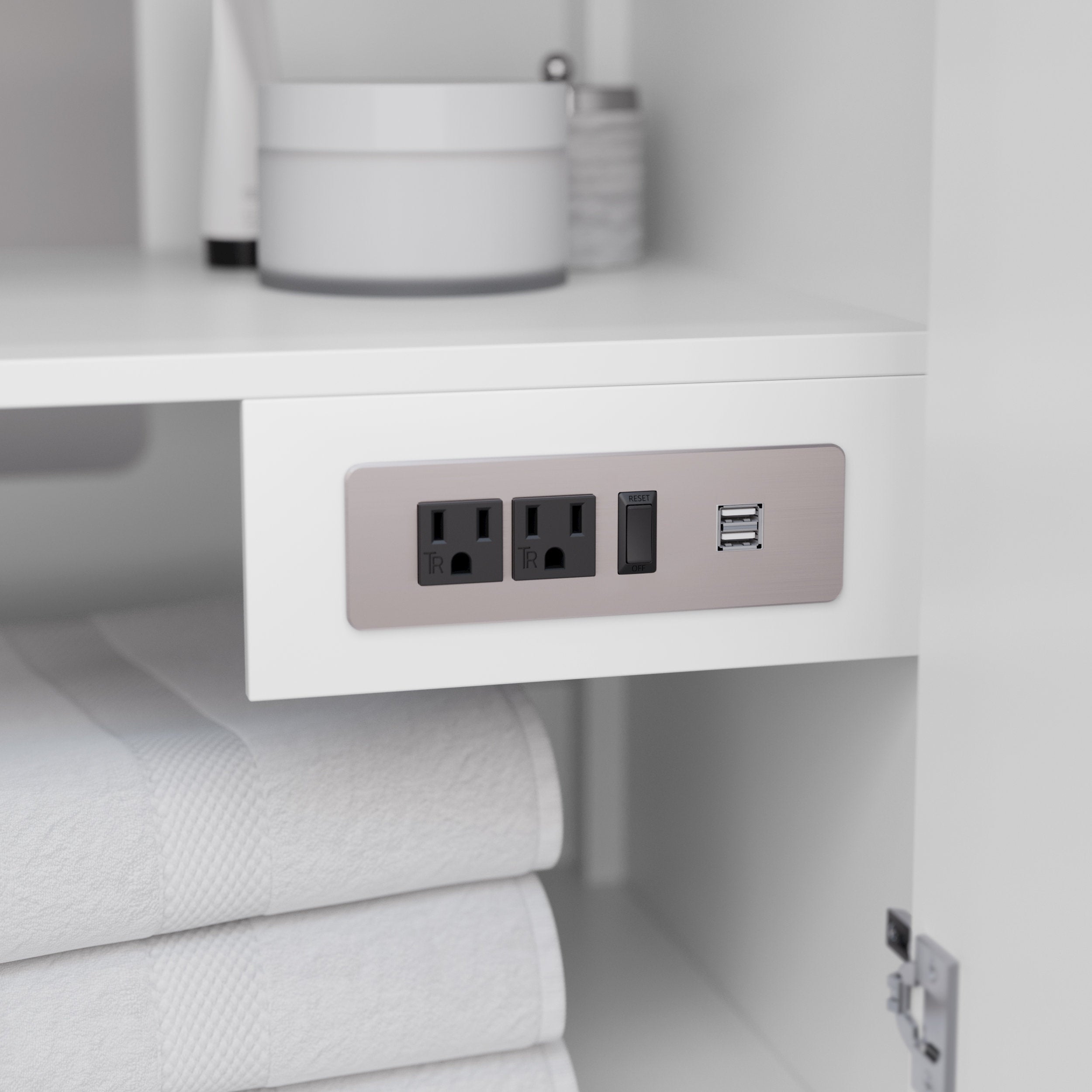 Close-up of a white solid-wood vanity interior showing a brushed-nickel under-shelf power panel with two electrical outlets, a reset switch and dual USB ports above folded white towels.